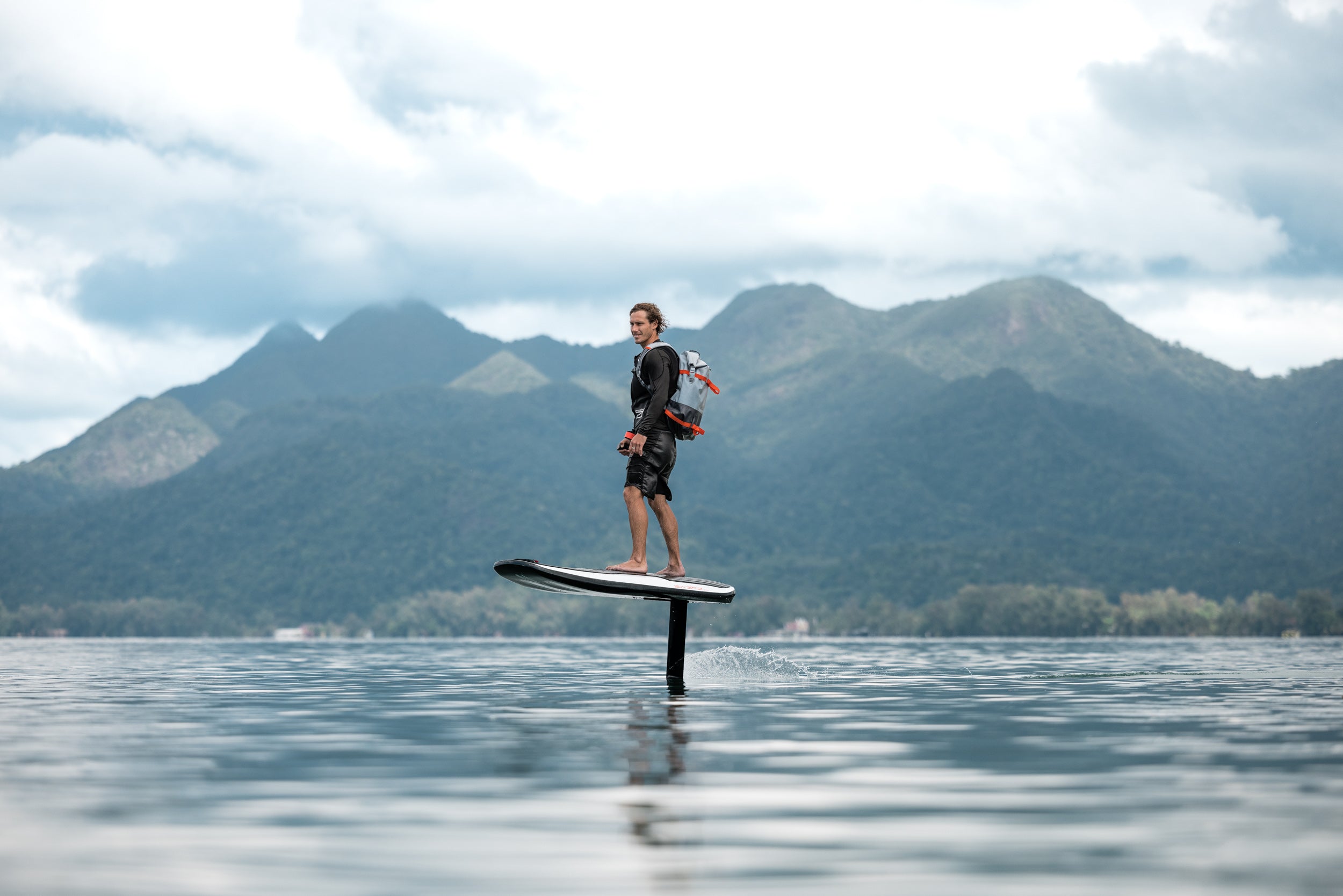 A man riding the Awake VINGA 3 eFoil with against the backdrop of green mountains.