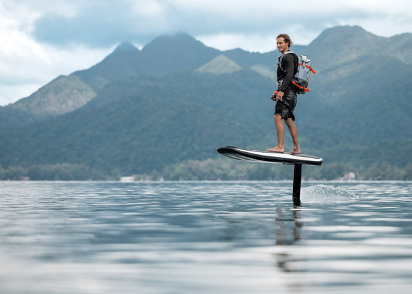 A man is soaring above the water on an Awake VINGA 3 efoil against a backdrop of lush green mountains in Thailand.