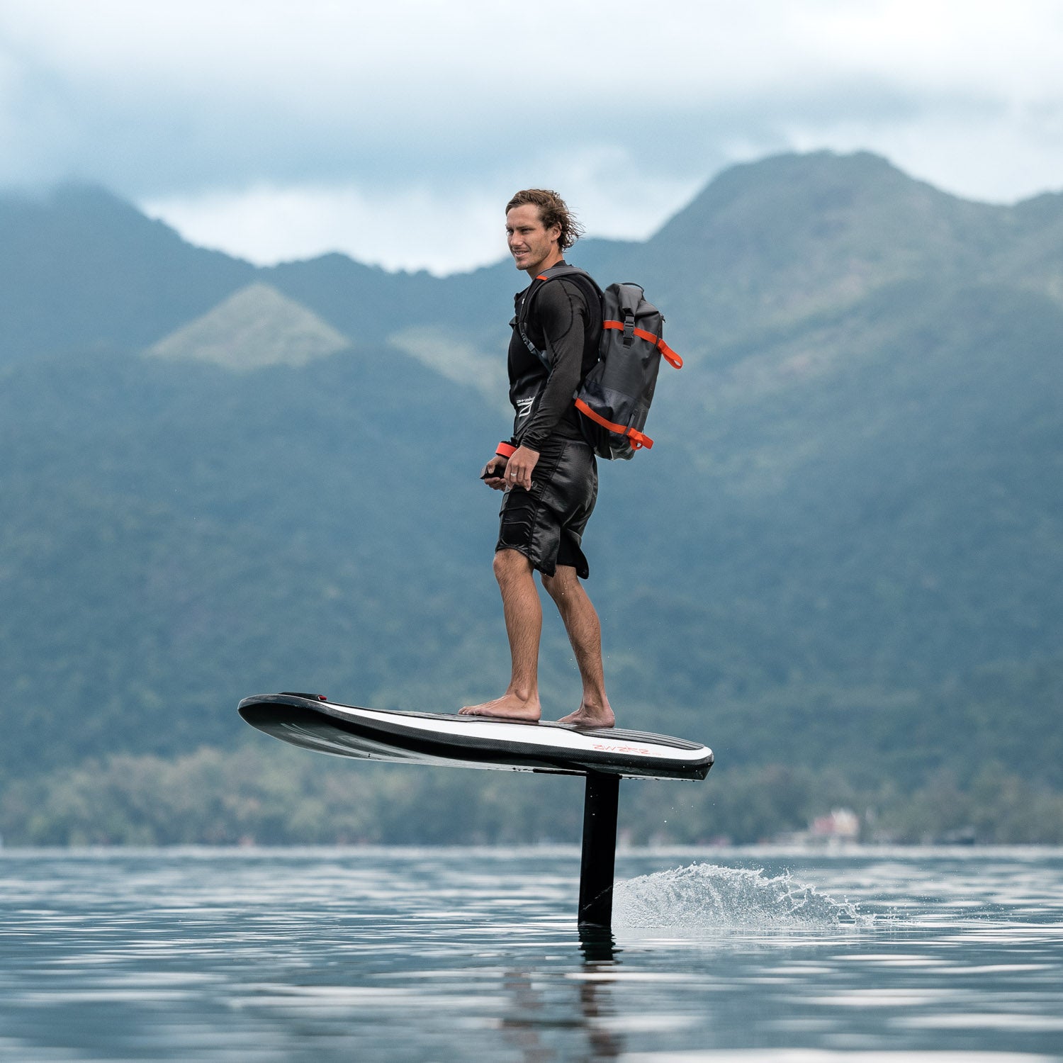 A man is soaring above the water on an Awake VINGA 3 efoil against a backdrop of lush green mountains in Thailand.